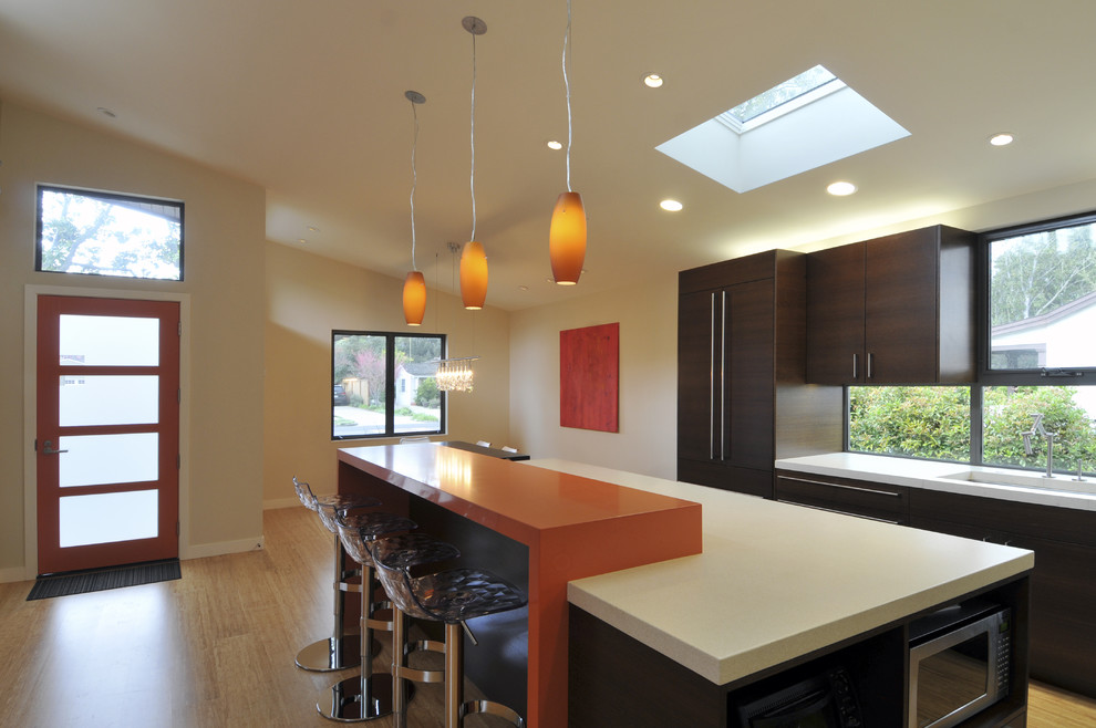 This is an example of a contemporary single-wall open plan kitchen in San Francisco with flat-panel cabinets, dark wood cabinets, engineered stone countertops, a submerged sink, bamboo flooring and an island.