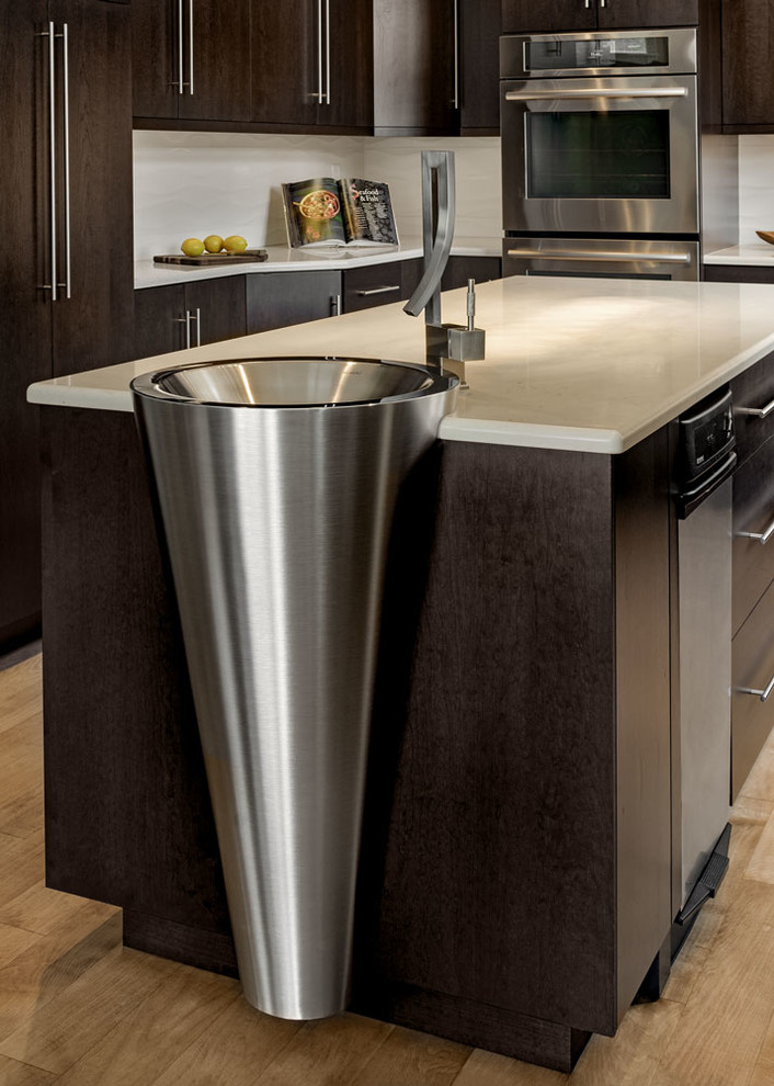 Photo of a medium sized contemporary u-shaped enclosed kitchen in Portland Maine with flat-panel cabinets, dark wood cabinets, beige splashback, stainless steel appliances, an island, marble worktops, porcelain splashback, a submerged sink and light hardwood flooring.