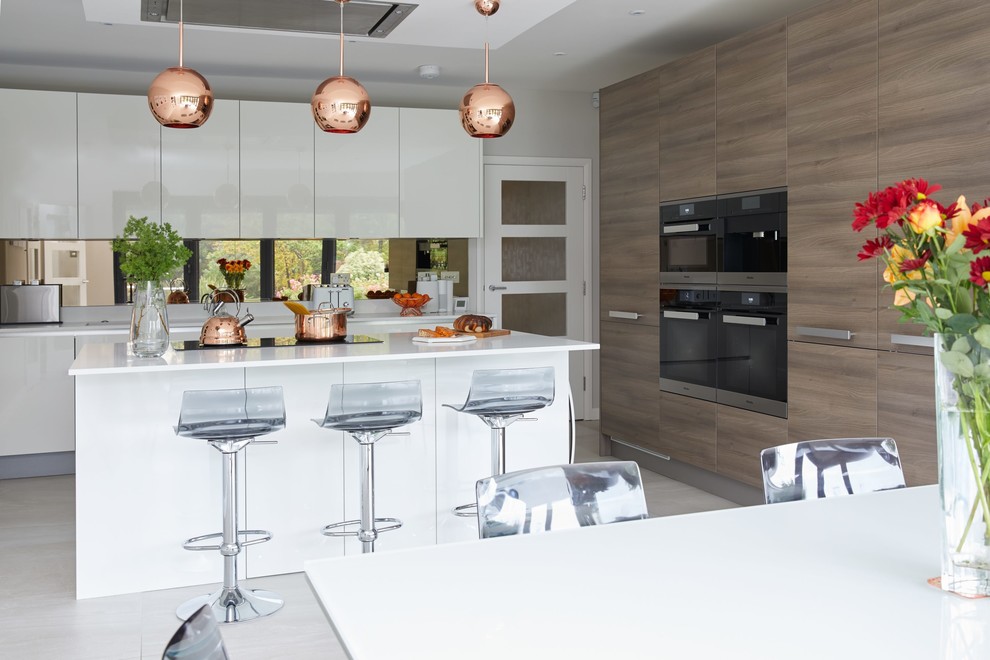 Photo of a large contemporary single-wall kitchen/diner in Hertfordshire with flat-panel cabinets, white cabinets, mirror splashback, stainless steel appliances, an island, grey floors and white worktops.