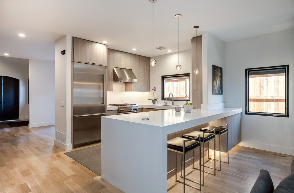 Photo of a medium sized contemporary u-shaped open plan kitchen in Denver with a submerged sink, flat-panel cabinets, grey cabinets, engineered stone countertops, white splashback, stainless steel appliances, light hardwood flooring, an island and brown floors.
