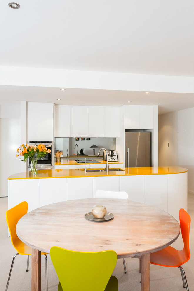 Inspiration för små moderna gult kök, med en undermonterad diskho, släta luckor, vita skåp, bänkskiva i kvarts, glaspanel som stänkskydd och rostfria vitvaror