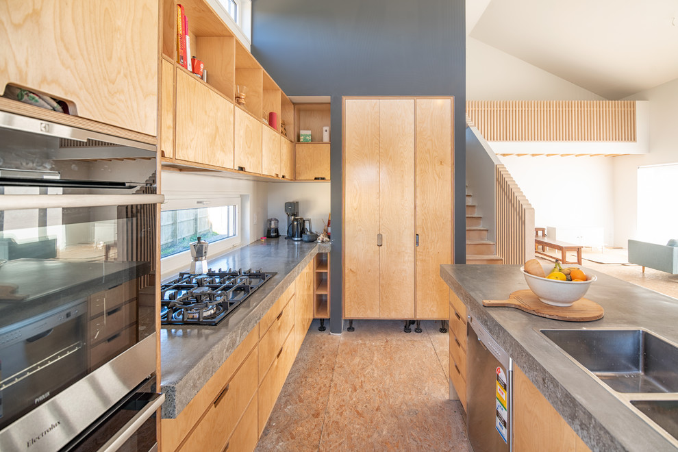 Immagine di una cucina minimal con lavello da incasso, ante lisce, ante in legno chiaro, top in cemento, elettrodomestici neri, pavimento in compensato, pavimento beige e top grigio