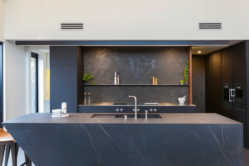 Foto på ett mellanstort funkis kök, med en köksö, en undermonterad diskho, släta luckor, svarta skåp, svart stänkskydd, stänkskydd i porslinskakel, rostfria vitvaror, klinkergolv i porslin och svart golv
