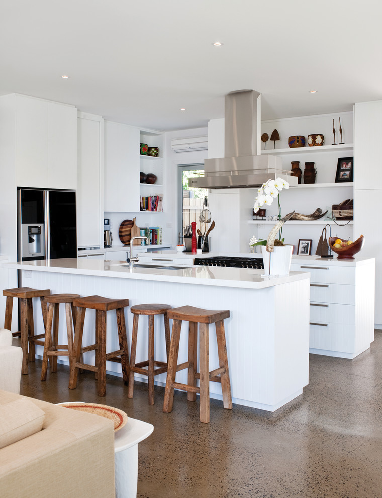 Стильный дизайн: угловая кухня-гостиная в современном стиле с двойной мойкой, плоскими фасадами, белыми фасадами, бетонным полом, островом и коричневым полом - последний тренд