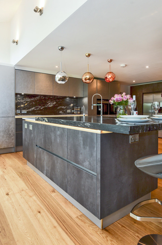 Photo of a large contemporary l-shaped kitchen/diner in Berkshire with flat-panel cabinets, grey cabinets, granite worktops, black splashback, stone slab splashback, integrated appliances, an island and black worktops.