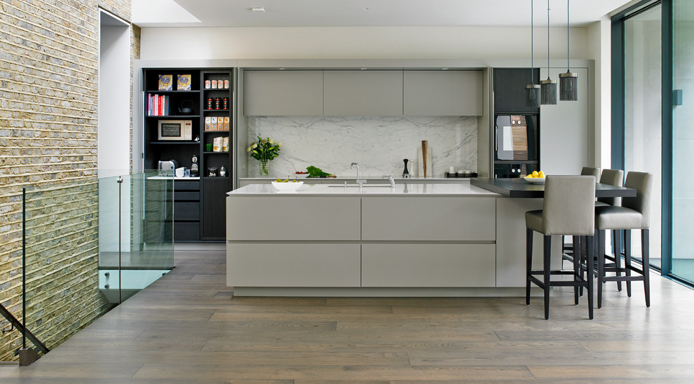 Contemporary kitchen in London with a submerged sink, flat-panel cabinets, grey cabinets, white splashback, black appliances, medium hardwood flooring and an island.