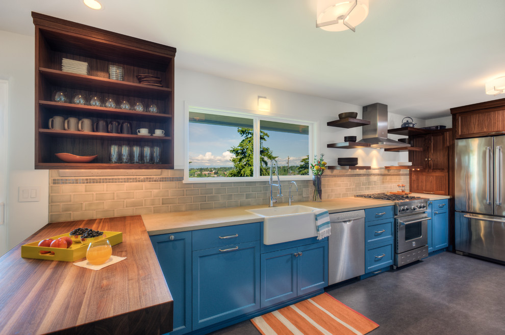 Photo of a large contemporary u-shaped kitchen/diner in Seattle with a belfast sink, shaker cabinets, blue cabinets, wood worktops, grey splashback, metro tiled splashback, stainless steel appliances, concrete flooring and a breakfast bar.