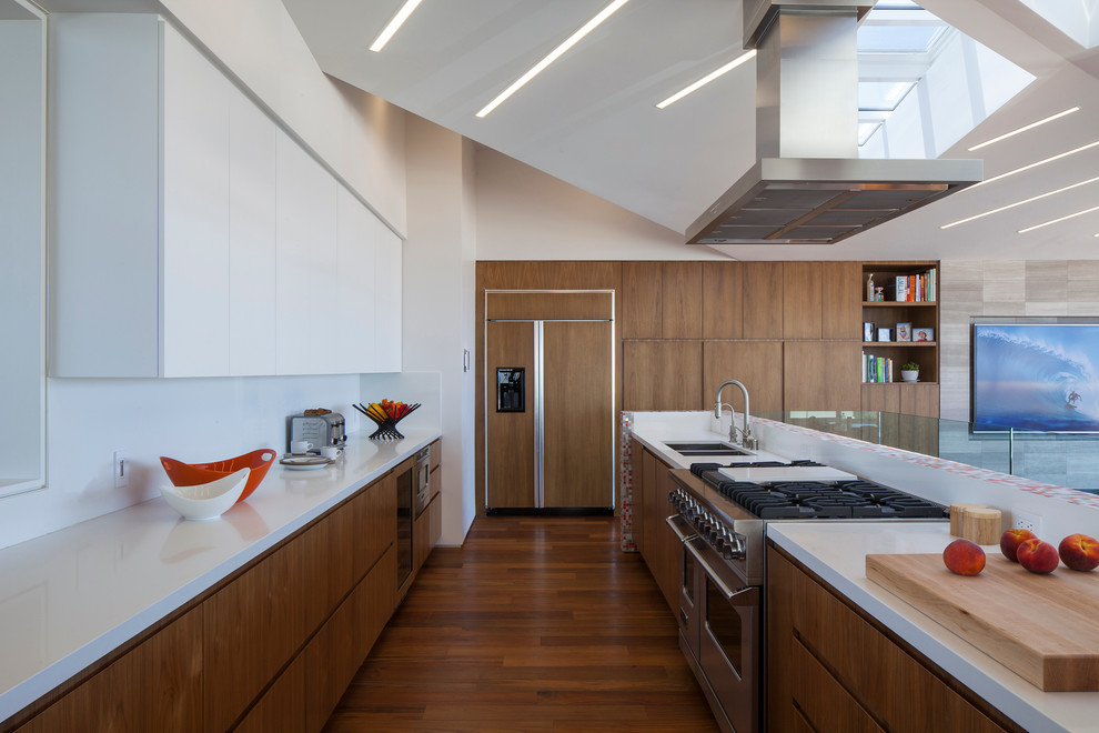 ロサンゼルスにあるコンテンポラリースタイルのおしゃれなキッチン (アンダーカウンターシンク、フラットパネル扉のキャビネット、中間色木目調キャビネット、白いキッチンパネル、シルバーの調理設備、無垢フローリング) の写真