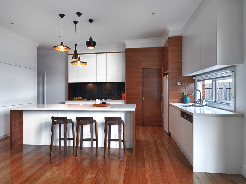 Photo of a medium sized contemporary l-shaped kitchen/diner in Melbourne with a submerged sink, flat-panel cabinets, medium wood cabinets, engineered stone countertops, grey splashback, glass sheet splashback, stainless steel appliances, medium hardwood flooring and an island.