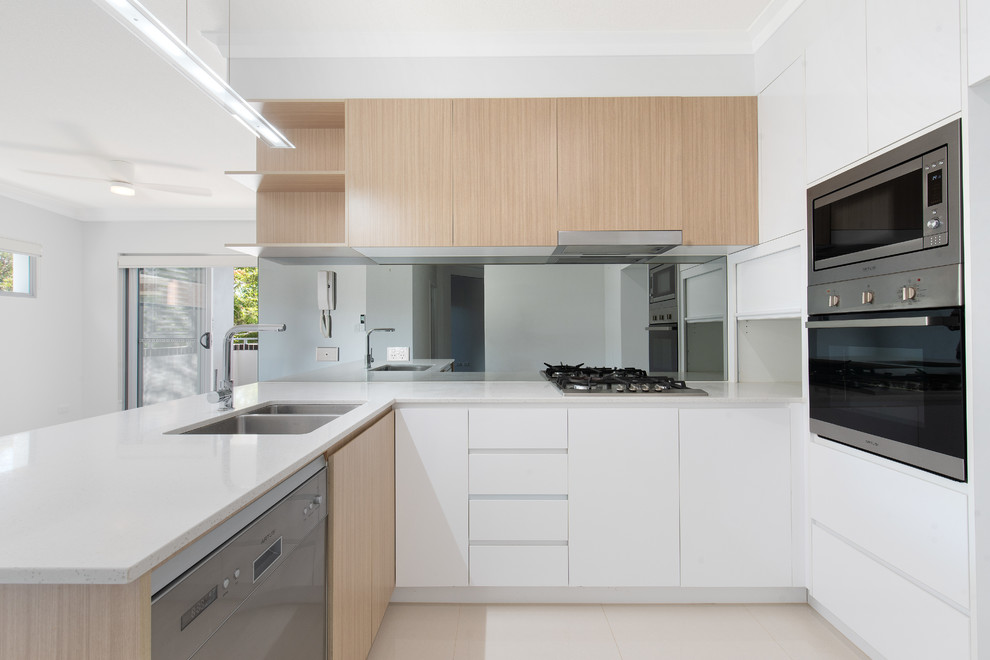 Moderne Küche in U-Form mit Doppelwaschbecken, flächenbündigen Schrankfronten, weißen Schränken, Rückwand aus Spiegelfliesen, Küchengeräten aus Edelstahl, Halbinsel, beigem Boden und weißer Arbeitsplatte in Brisbane