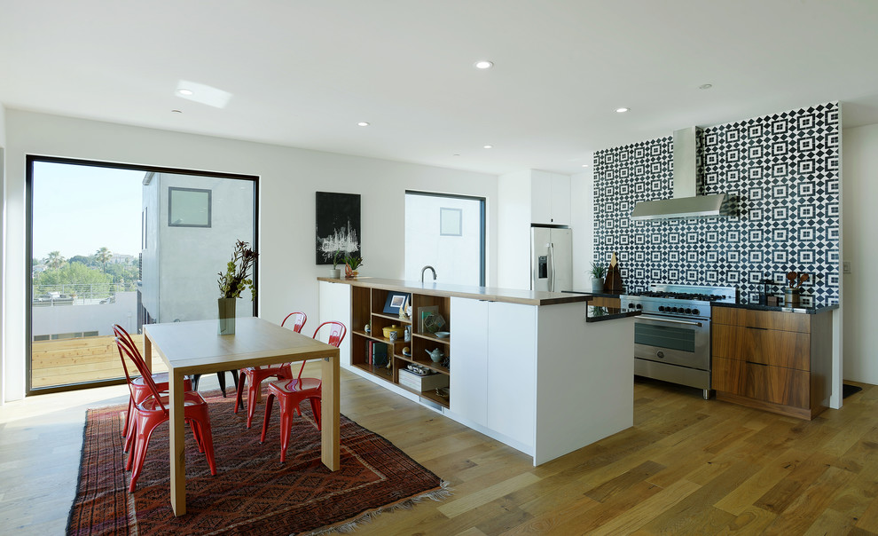Zweizeilige Moderne Wohnküche mit flächenbündigen Schrankfronten, dunklen Holzschränken, bunter Rückwand, Küchengeräten aus Edelstahl, braunem Holzboden und Kücheninsel in Los Angeles