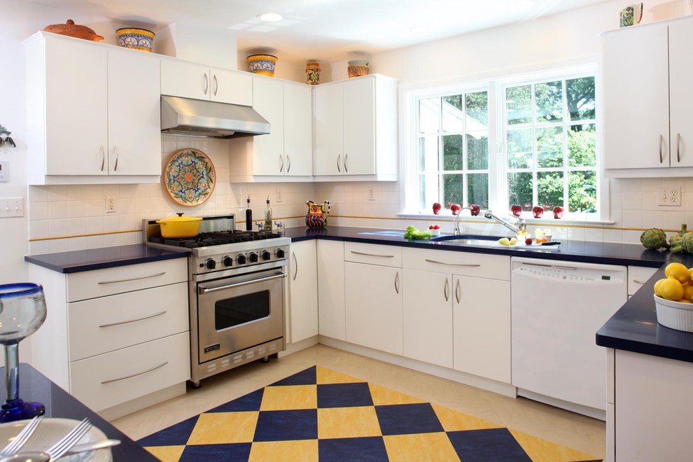 Cette photo montre une cuisine tendance en U avec un placard à porte plane, des portes de placard blanches, une crédence blanche, un électroménager en acier inoxydable et fenêtre au-dessus de l'évier.
