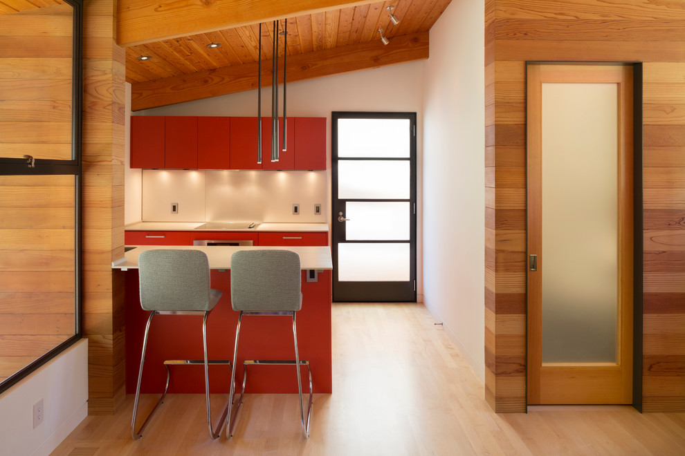Modelo de cocina contemporánea pequeña con armarios con paneles lisos, puertas de armario rojas, suelo de madera clara y península