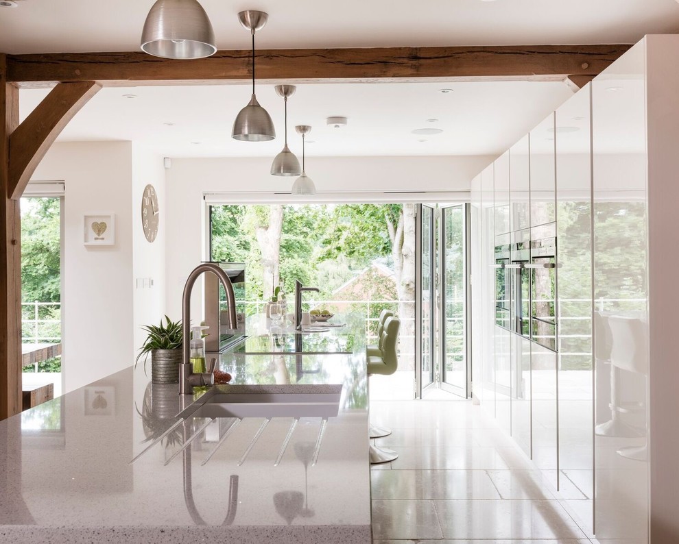 Modern inredning av ett mellanstort kök, med en undermonterad diskho, släta luckor, vita skåp, granitbänkskiva, rostfria vitvaror, en köksö och vitt golv