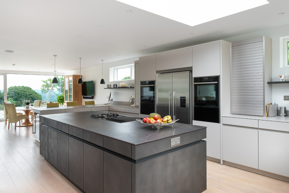 Inredning av ett modernt stort grå grått kök och matrum, med släta luckor, grå skåp, rostfria vitvaror, ljust trägolv, en köksö och beiget golv