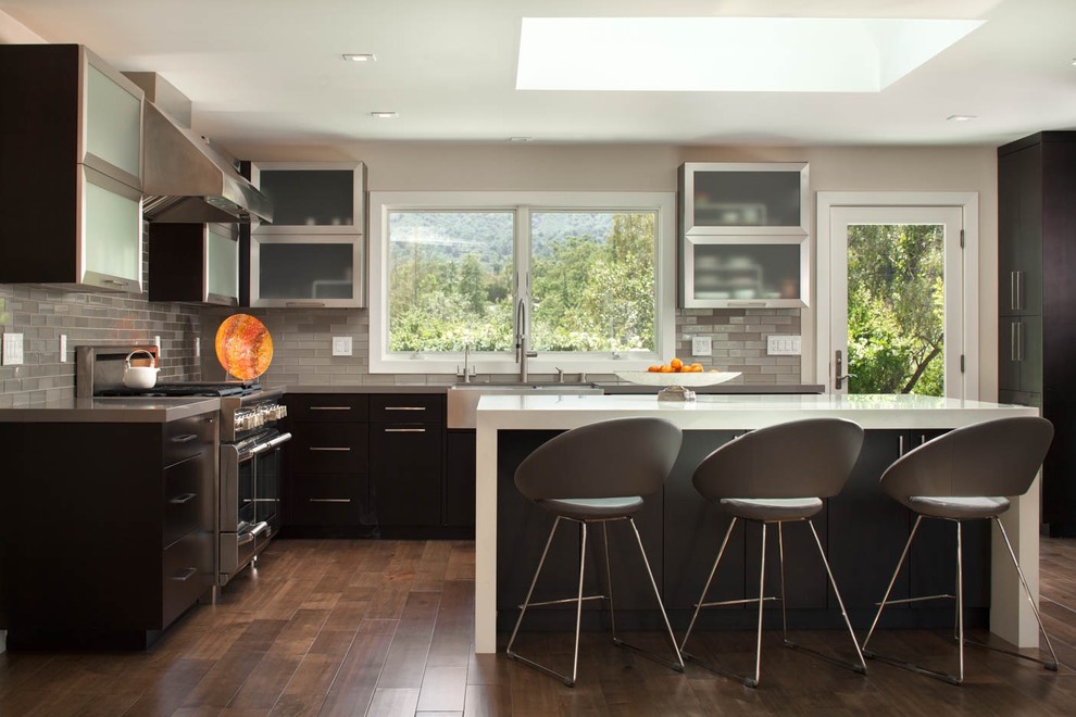 サンフランシスコにあるコンテンポラリースタイルのおしゃれなキッチン (エプロンフロントシンク、ガラス扉のキャビネット、濃色木目調キャビネット、ベージュキッチンパネル、シルバーの調理設備、無垢フローリング、茶色い床) の写真