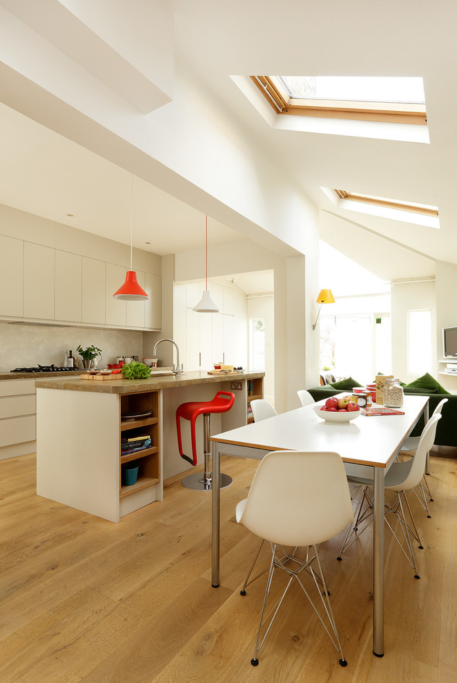На фото: параллельная кухня-гостиная в современном стиле с плоскими фасадами, бежевыми фасадами, бежевым фартуком, светлым паркетным полом и островом с