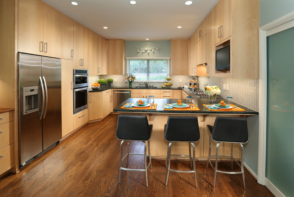 This is an example of a medium sized contemporary u-shaped kitchen/diner in Los Angeles with a submerged sink, flat-panel cabinets, light wood cabinets, soapstone worktops, glass tiled splashback, stainless steel appliances, medium hardwood flooring and a breakfast bar.
