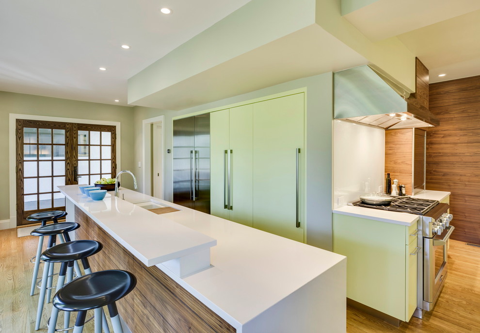 Modern inredning av ett kök, med en undermonterad diskho, släta luckor, gröna skåp, bänkskiva i kvarts, vitt stänkskydd och rostfria vitvaror