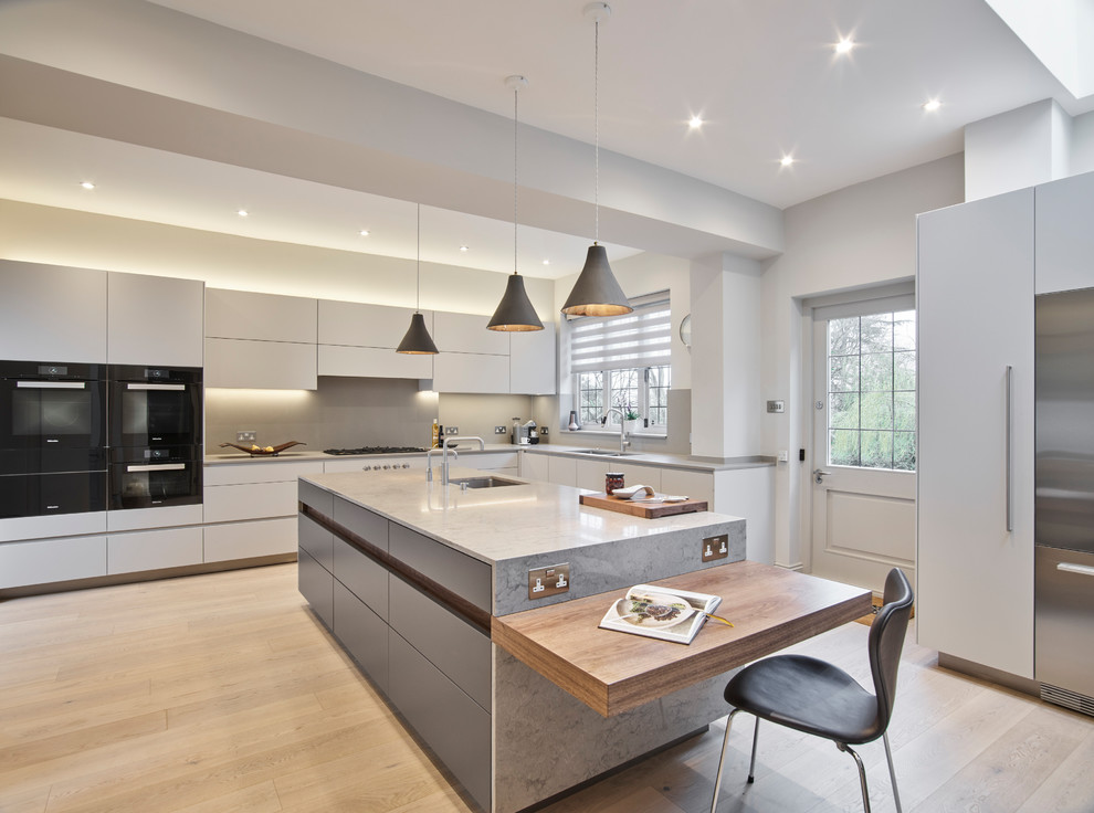 Photo of a contemporary l-shaped kitchen in London with a submerged sink, flat-panel cabinets, white cabinets, grey splashback, stainless steel appliances, light hardwood flooring, an island and beige floors.