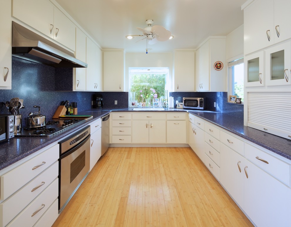 Geschlossene Moderne Küche mit flächenbündigen Schrankfronten, weißen Schränken, Küchenrückwand in Schwarz, Rückwand aus Stein und blauer Arbeitsplatte