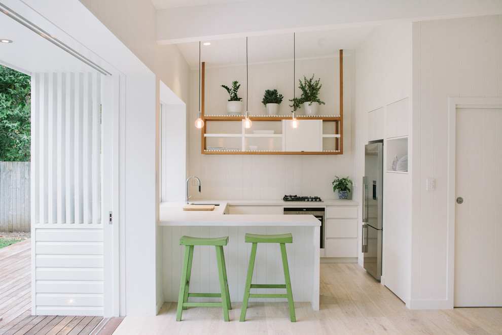 Photo of a small contemporary u-shaped kitchen in Other with a submerged sink, flat-panel cabinets, white cabinets, stainless steel appliances and light hardwood flooring.