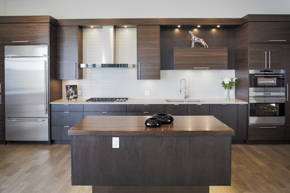 Mittelgroße Moderne Küche mit Unterbauwaschbecken, flächenbündigen Schrankfronten, braunen Schränken, Granit-Arbeitsplatte, Rückwand aus Glasfliesen, Küchengeräten aus Edelstahl, hellem Holzboden und zwei Kücheninseln in Calgary