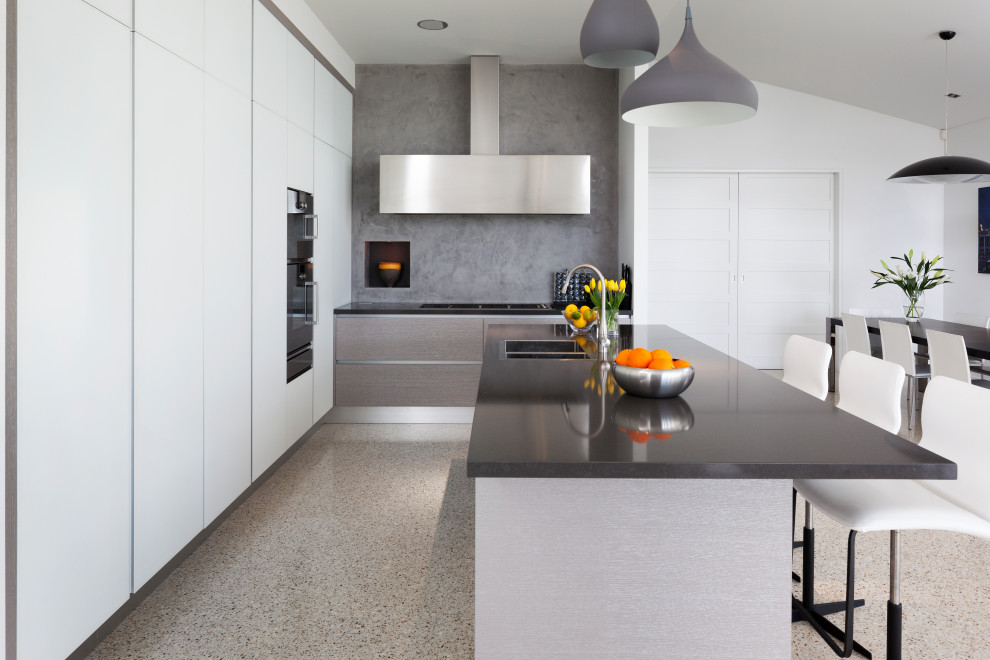 Photo of a large contemporary l-shaped kitchen/diner in Perth with an integrated sink, flat-panel cabinets, composite countertops, grey splashback, mosaic tiled splashback, stainless steel appliances, terrazzo flooring, an island, beige floors and black worktops.