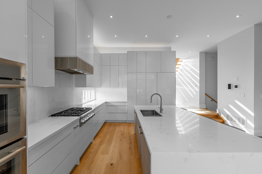Large trendy l-shaped light wood floor and beige floor eat-in kitchen photo in Toronto with an undermount sink, flat-panel cabinets, white cabinets, quartz countertops, white backsplash, quartz backsplash, paneled appliances, an island and white countertops