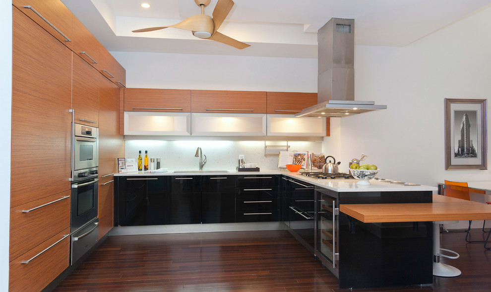 Modern inredning av ett kök, med en undermonterad diskho, släta luckor, skåp i mellenmörkt trä, rostfria vitvaror, mörkt trägolv och en halv köksö