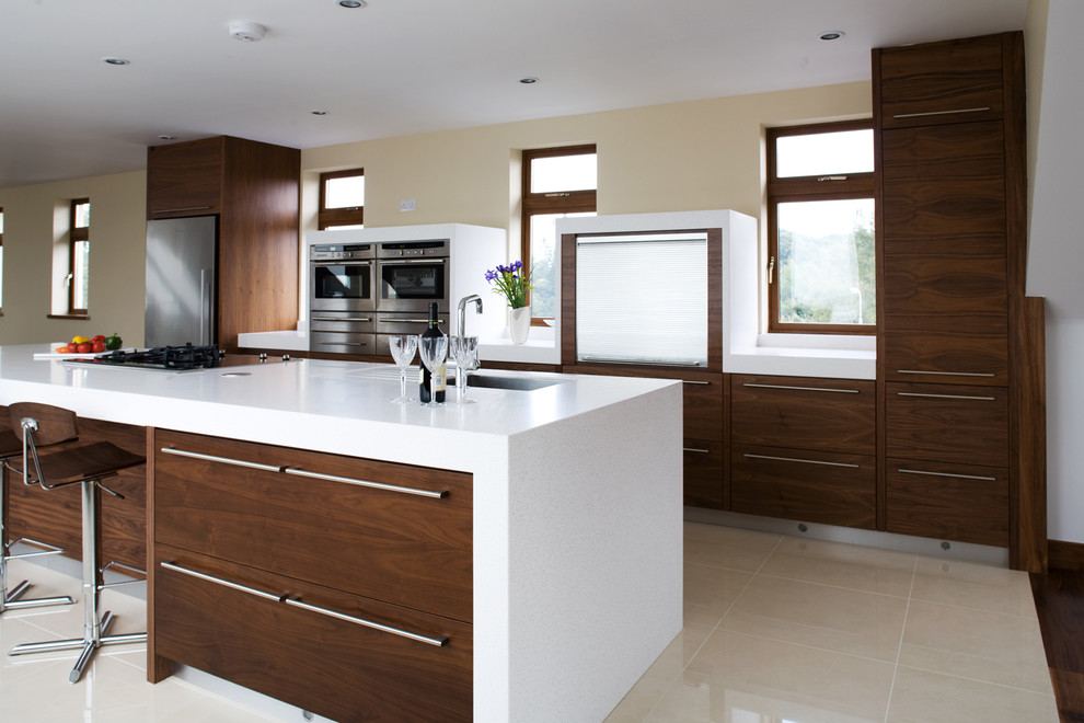 Diseño de cocina actual con armarios con paneles lisos, puertas de armario de madera en tonos medios, electrodomésticos de acero inoxidable, suelo beige y barras de cocina