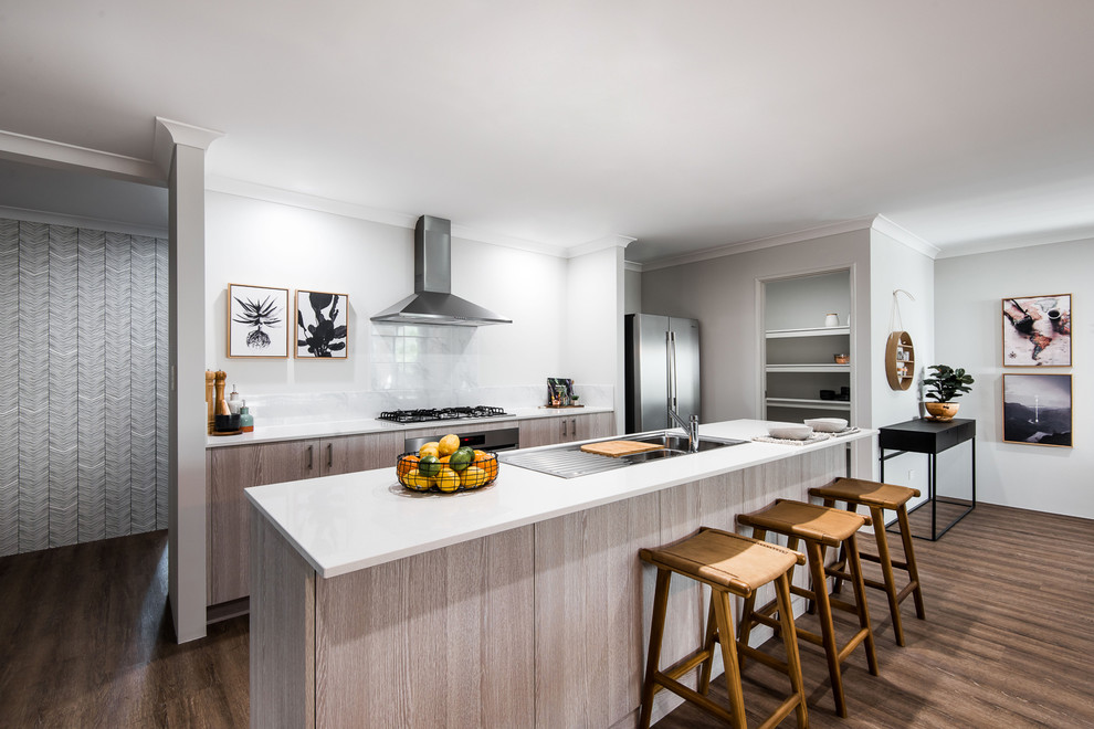 This is an example of a medium sized contemporary galley open plan kitchen in Perth with flat-panel cabinets, light wood cabinets, an island, a double-bowl sink, white splashback, stainless steel appliances, brown floors, engineered stone countertops, ceramic splashback and laminate floors.