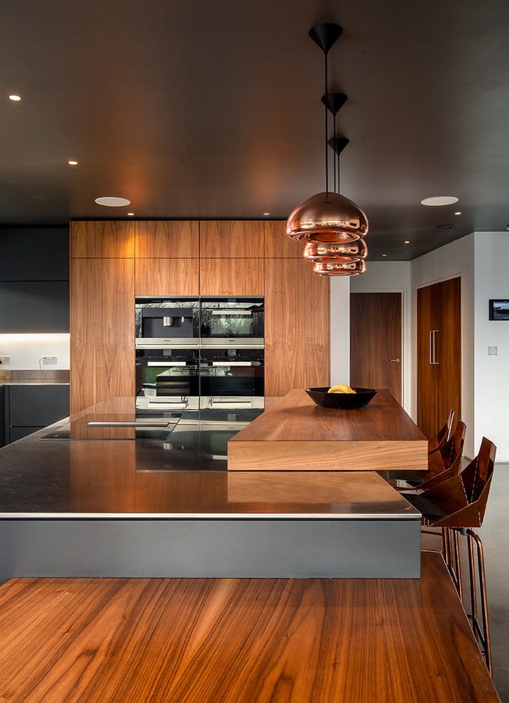 Foto på ett stort funkis kök och matrum, med släta luckor, skåp i mellenmörkt trä, bänkskiva i rostfritt stål, integrerade vitvaror, betonggolv, en köksö och grått golv