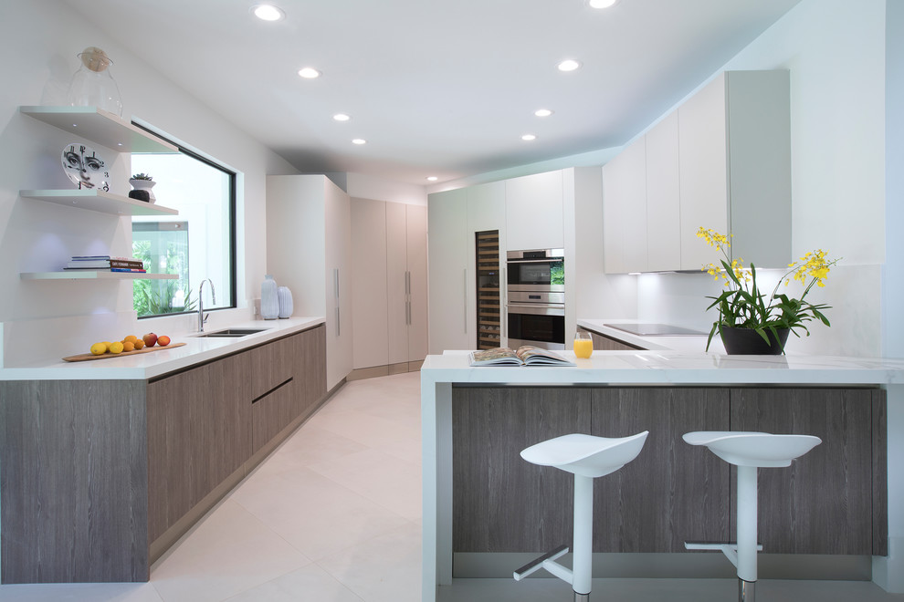 Moderne Küche in U-Form mit Doppelwaschbecken, flächenbündigen Schrankfronten, grauen Schränken, Rückwand-Fenster, Küchengeräten aus Edelstahl und Halbinsel in Miami