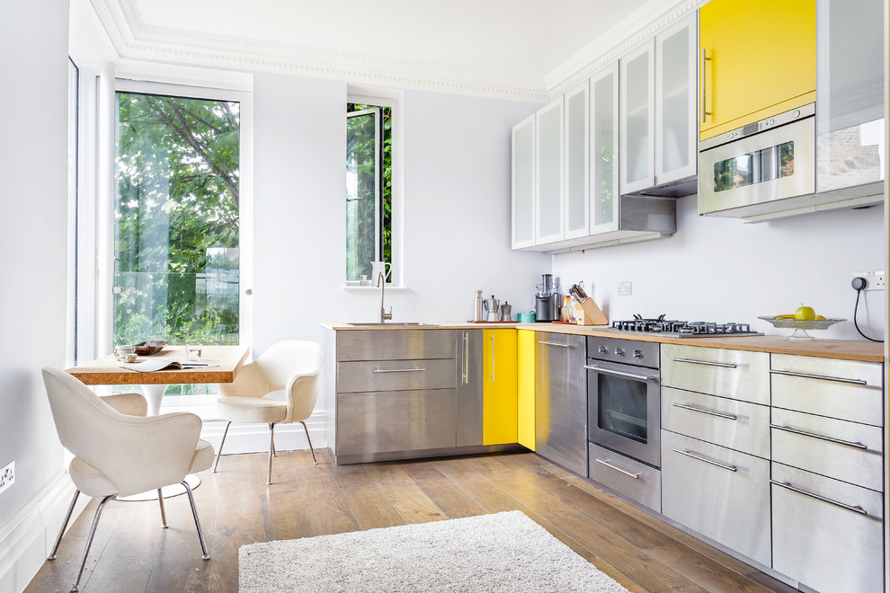 Contemporary l-shaped kitchen/diner in London with a built-in sink, flat-panel cabinets, stainless steel cabinets, wood worktops, stainless steel appliances, light hardwood flooring and no island.