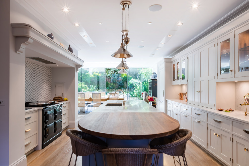 Large traditional kitchen/diner in London with grey cabinets, multi-coloured splashback, ceramic splashback, black appliances, an island, marble worktops, light hardwood flooring, beige floors, a single-bowl sink and glass-front cabinets.