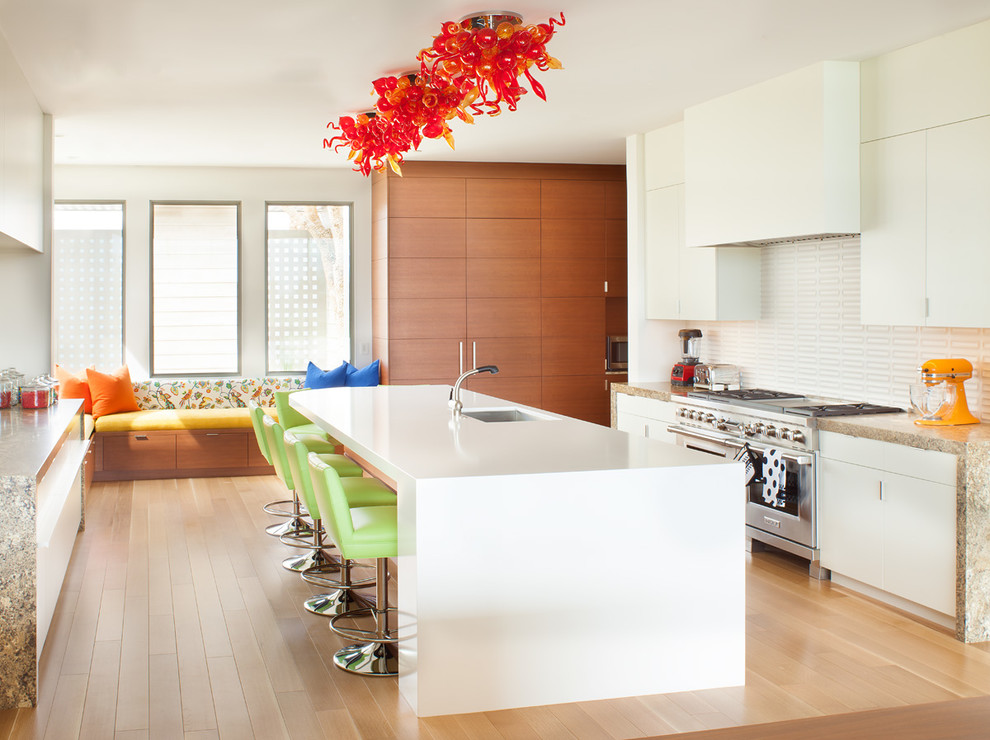 Photo of a medium sized contemporary u-shaped open plan kitchen in Los Angeles with a submerged sink, flat-panel cabinets, white cabinets, white splashback, stainless steel appliances, light hardwood flooring, an island, composite countertops and ceramic splashback.