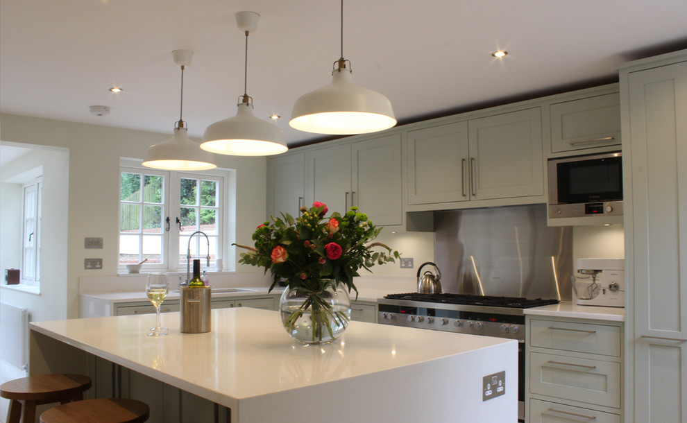 This is an example of a contemporary open plan kitchen in Surrey with shaker cabinets, grey cabinets, composite countertops, stainless steel appliances and a breakfast bar.