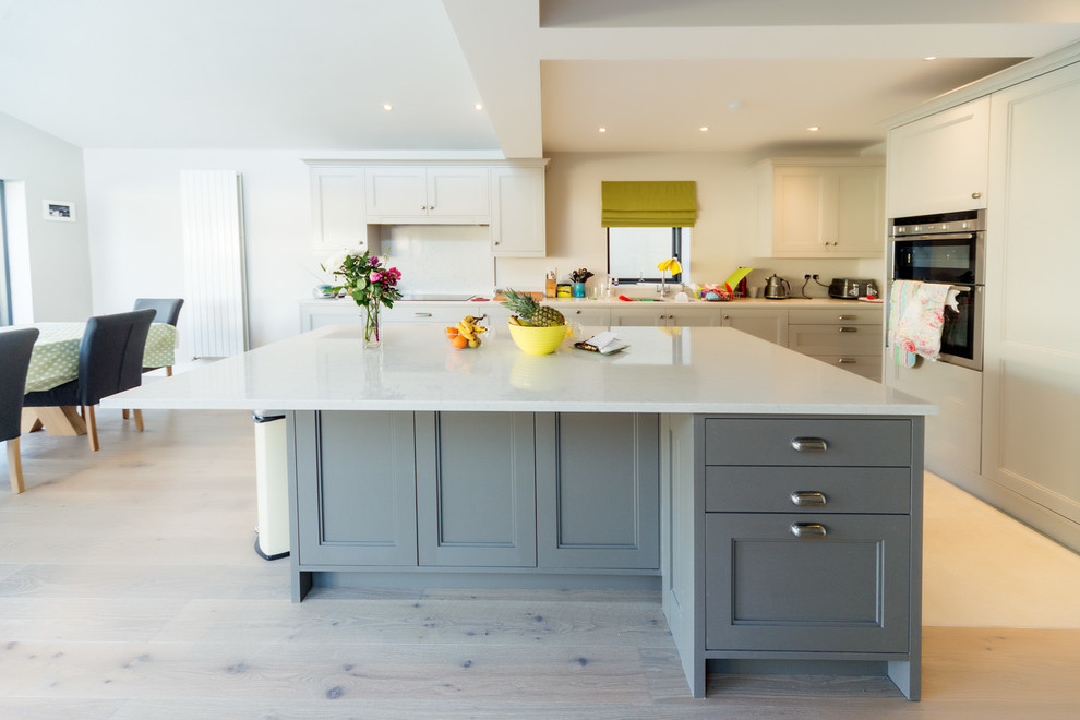 Inspiration for a classic kitchen/diner in Dublin with recessed-panel cabinets, grey cabinets, light hardwood flooring, an island, white splashback, stainless steel appliances and beige floors.