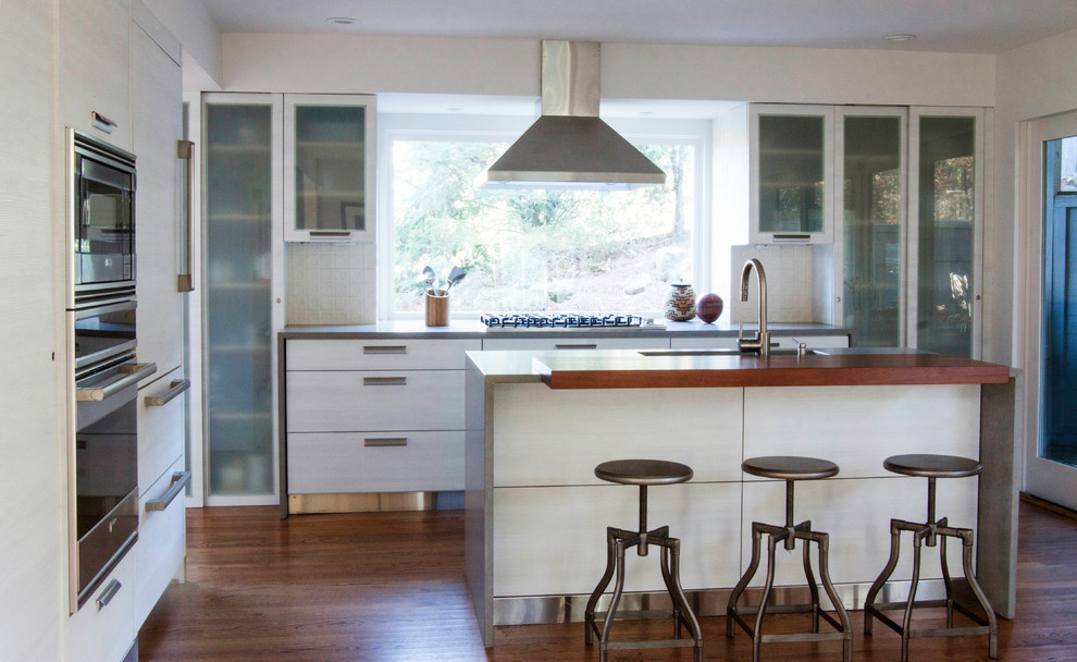Photo of a medium sized contemporary l-shaped kitchen/diner in Atlanta with a submerged sink, flat-panel cabinets, white cabinets, concrete worktops, white splashback, ceramic splashback, stainless steel appliances, dark hardwood flooring and an island.