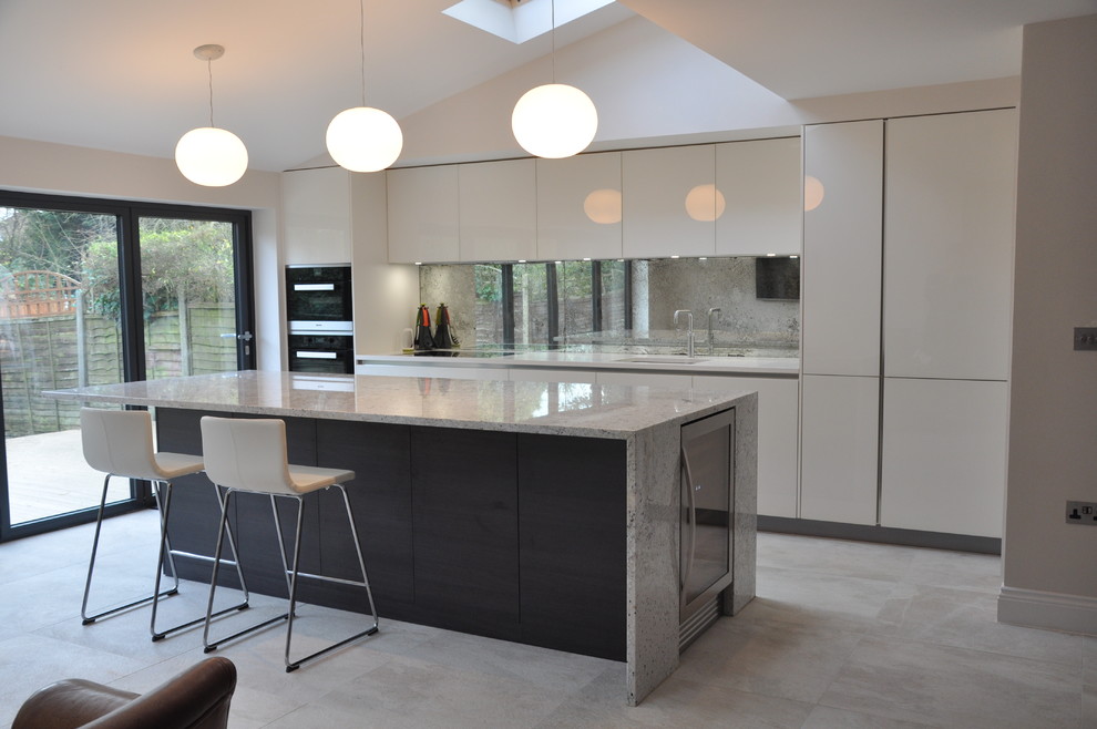 Offene Moderne Küche in L-Form mit flächenbündigen Schrankfronten, Rückwand aus Spiegelfliesen, Küchengeräten aus Edelstahl, Kücheninsel und weißen Schränken in Hertfordshire