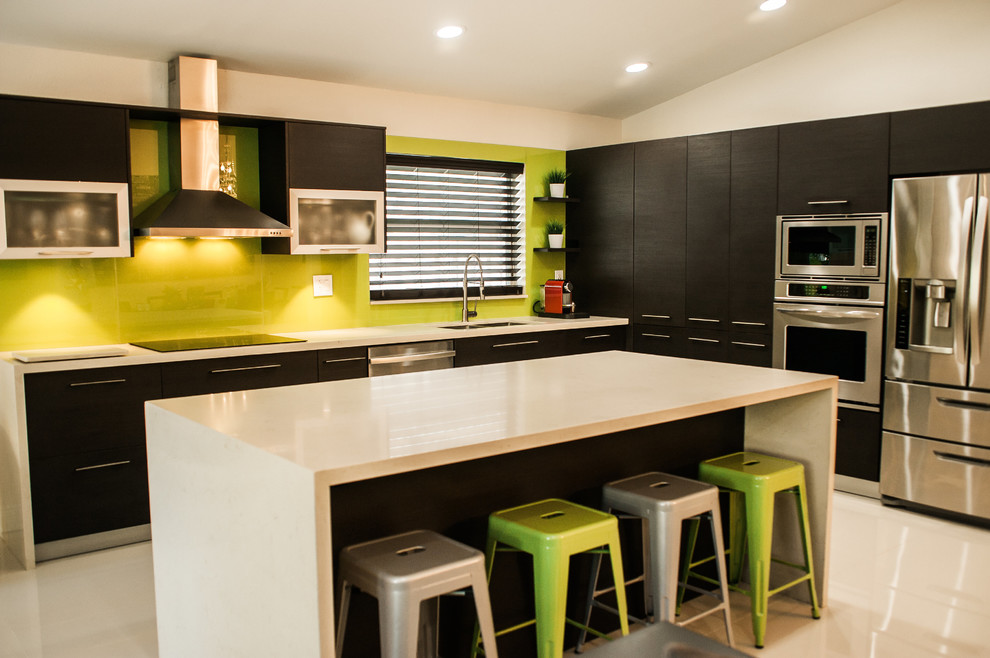 Example of a mid-sized trendy l-shaped concrete floor enclosed kitchen design in Miami with an undermount sink, flat-panel cabinets, dark wood cabinets, quartz countertops, green backsplash, glass sheet backsplash, stainless steel appliances and an island