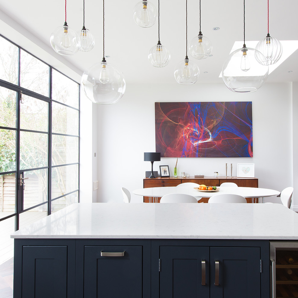 Photo of a medium sized contemporary open plan kitchen in London with a belfast sink, shaker cabinets, grey cabinets, quartz worktops, ceramic splashback, stainless steel appliances, dark hardwood flooring and an island.