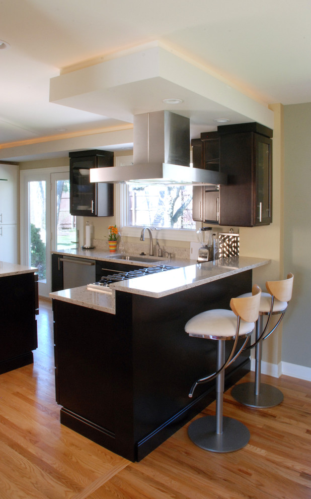 Cette photo montre une cuisine américaine tendance en bois foncé avec un évier 1 bac, un plan de travail en granite, un électroménager en acier inoxydable, un sol en bois brun et îlot.