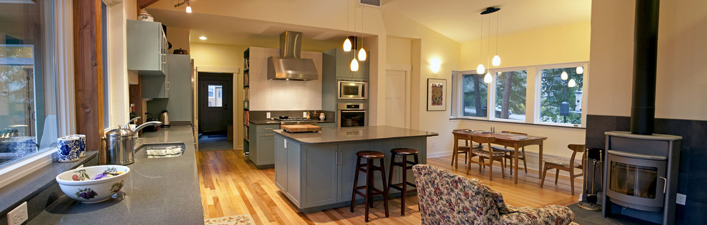 Exempel på ett stort modernt kök, med en undermonterad diskho, skåp i shakerstil, blå skåp, vitt stänkskydd, rostfria vitvaror, ljust trägolv, en köksö, granitbänkskiva och stänkskydd i porslinskakel