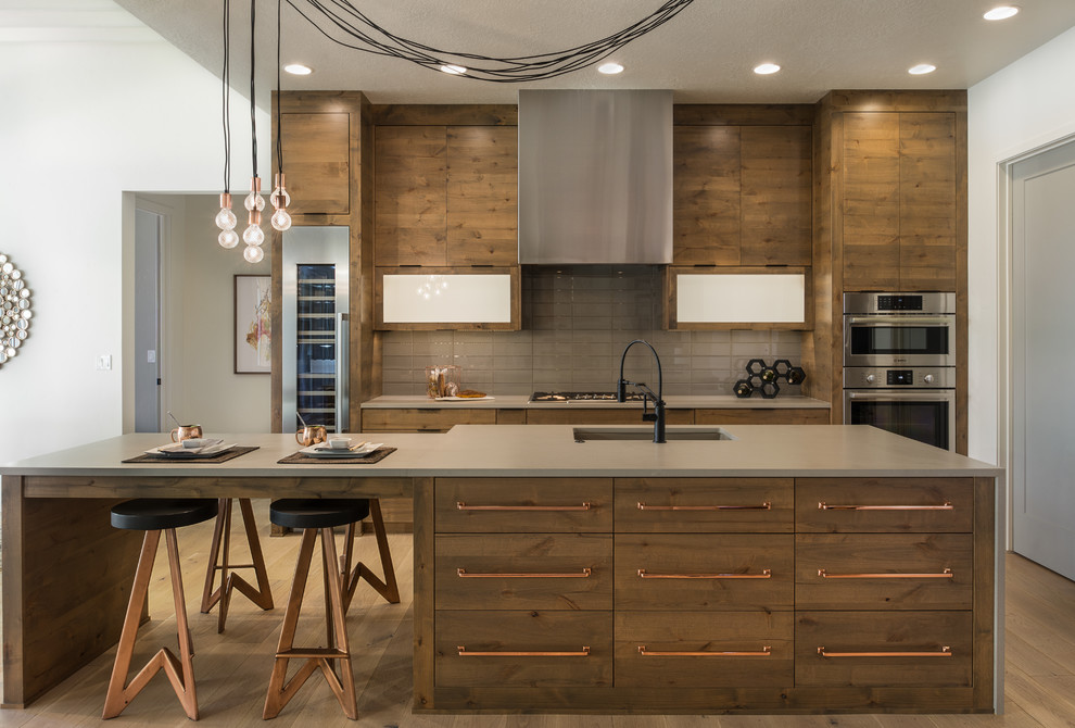 This is an example of a contemporary kitchen in Boise with a submerged sink, flat-panel cabinets, medium wood cabinets, grey splashback, stainless steel appliances, medium hardwood flooring and an island.