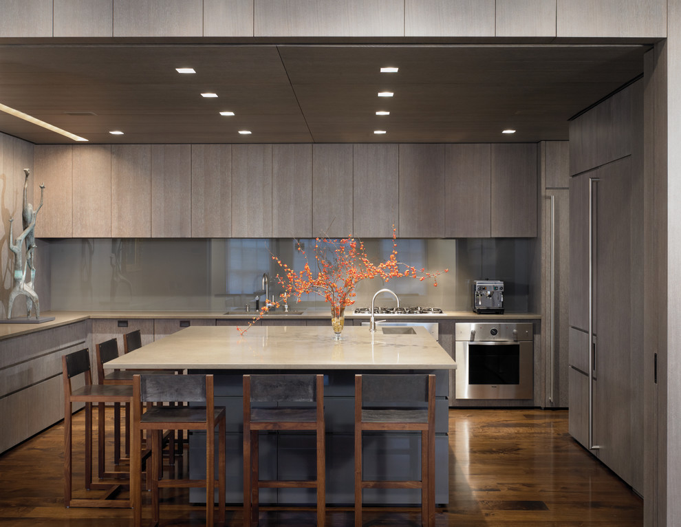 На фото: кухня в современном стиле с плоскими фасадами, серыми фасадами, серым фартуком, техникой под мебельный фасад и барной стойкой с