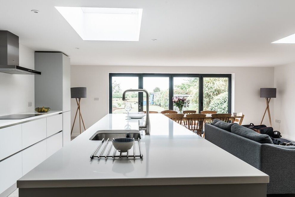 Photo of a large contemporary single-wall open plan kitchen in Oxfordshire with a built-in sink, flat-panel cabinets, grey cabinets, quartz worktops, integrated appliances, porcelain flooring, an island and beige floors.