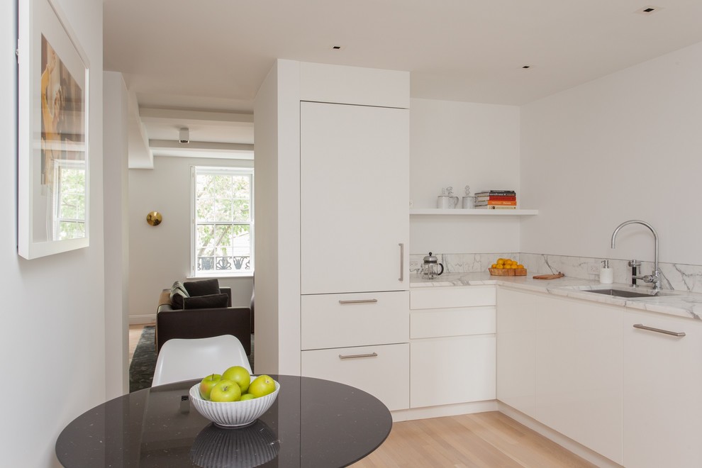 Photo of a small contemporary l-shaped enclosed kitchen in New York with a single-bowl sink, flat-panel cabinets, white cabinets, marble worktops, grey splashback, marble splashback, integrated appliances, light hardwood flooring, no island and brown floors.