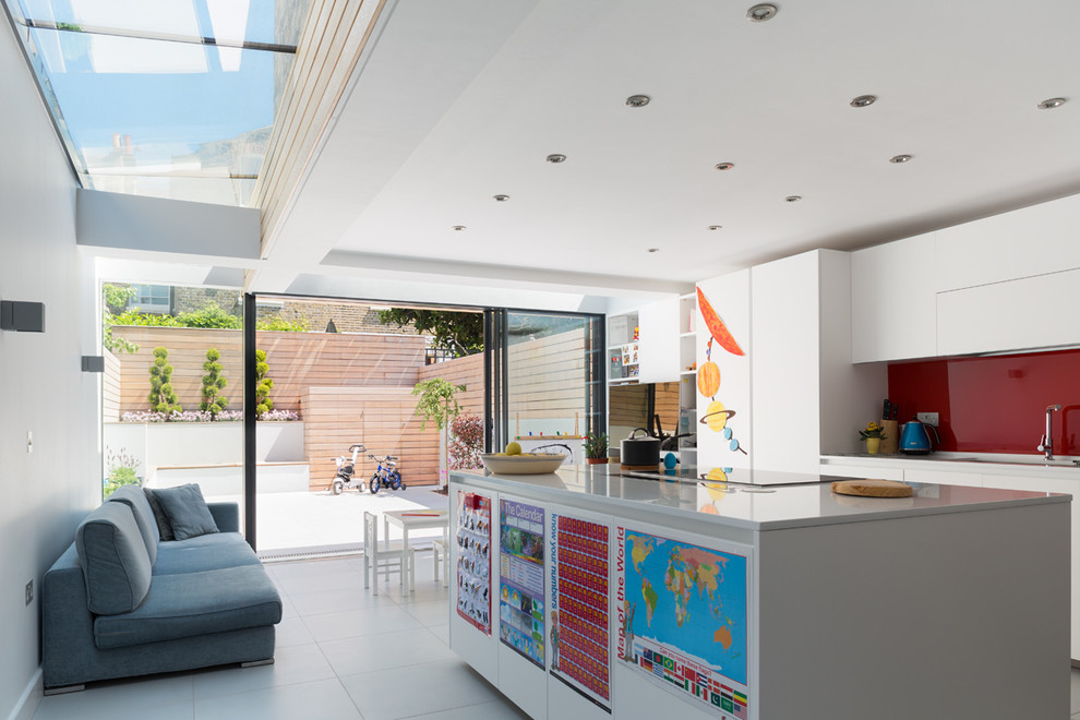 This is an example of a contemporary galley kitchen in London with an island, a submerged sink, flat-panel cabinets, white cabinets, red splashback and glass sheet splashback.
